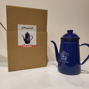 May include: A cobalt blue enamel kettle with a spout and handle, next to a cardboard box. The kettle has a logo that says "Valley of Witches". The box has Japanese text and a picture of the kettle.