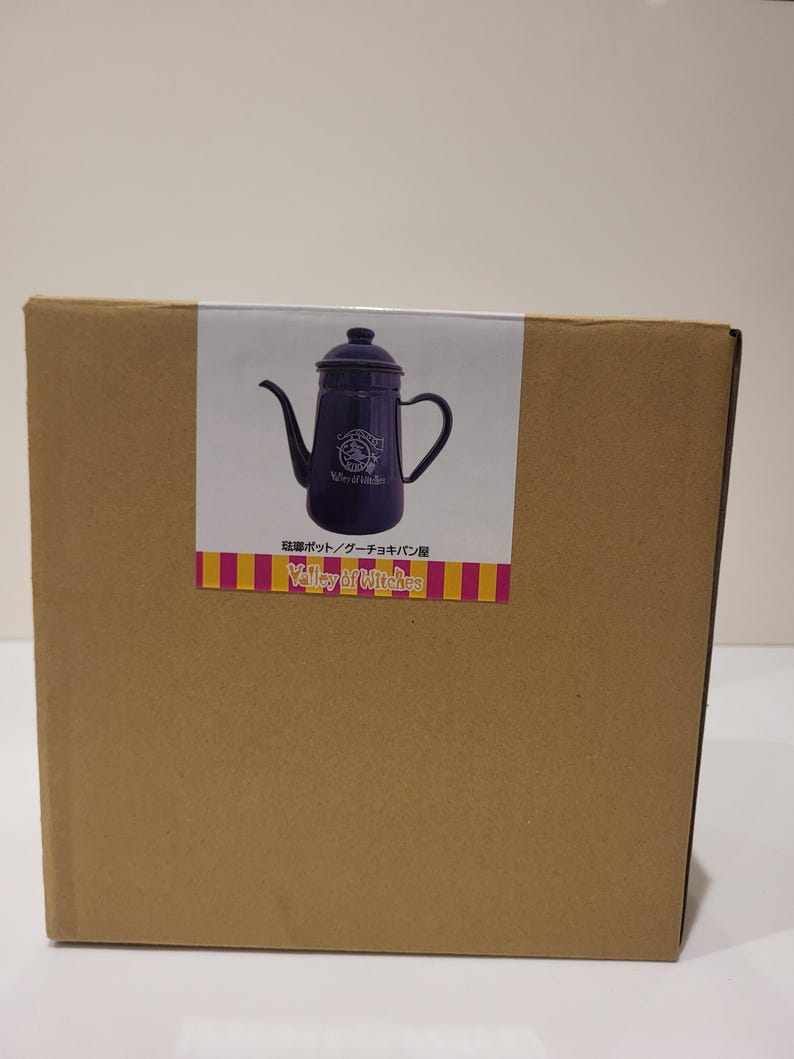 May include: A cardboard box with a sticker featuring a dark purple teapot with a long spout and handle. The sticker also includes the text "Valley of Witches" and Japanese text.