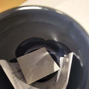 May include: A dark blue, glossy ceramic bowl with a white square card and a partially visible paper with Japanese text inside. The bowl's interior reflects light, highlighting its smooth surface.