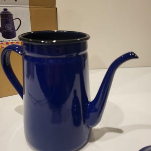May include: A cobalt blue enamel coffee pot with a long, curved spout and a black rim. The pot has a large handle and a matching lid. The design is simple and classic, suitable for brewing coffee.