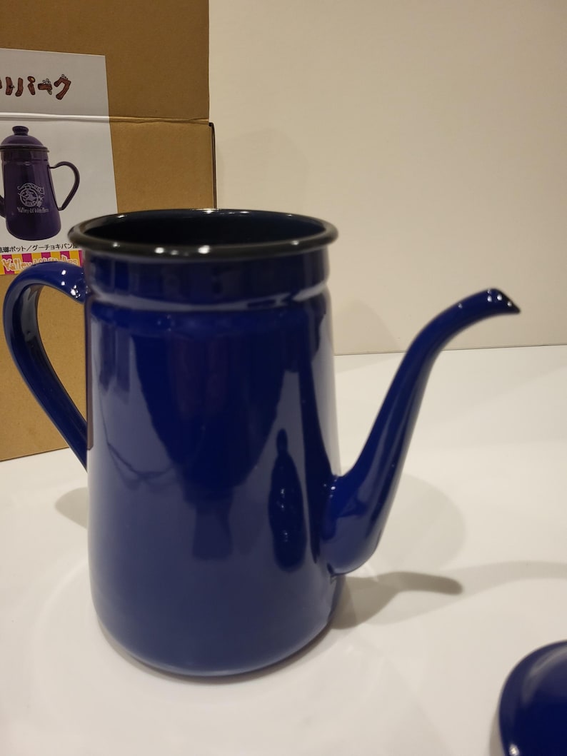 May include: A cobalt blue enamel coffee pot with a long, curved spout and a black rim. The pot has a large handle and a matching lid. The design is simple and classic, suitable for brewing coffee.
