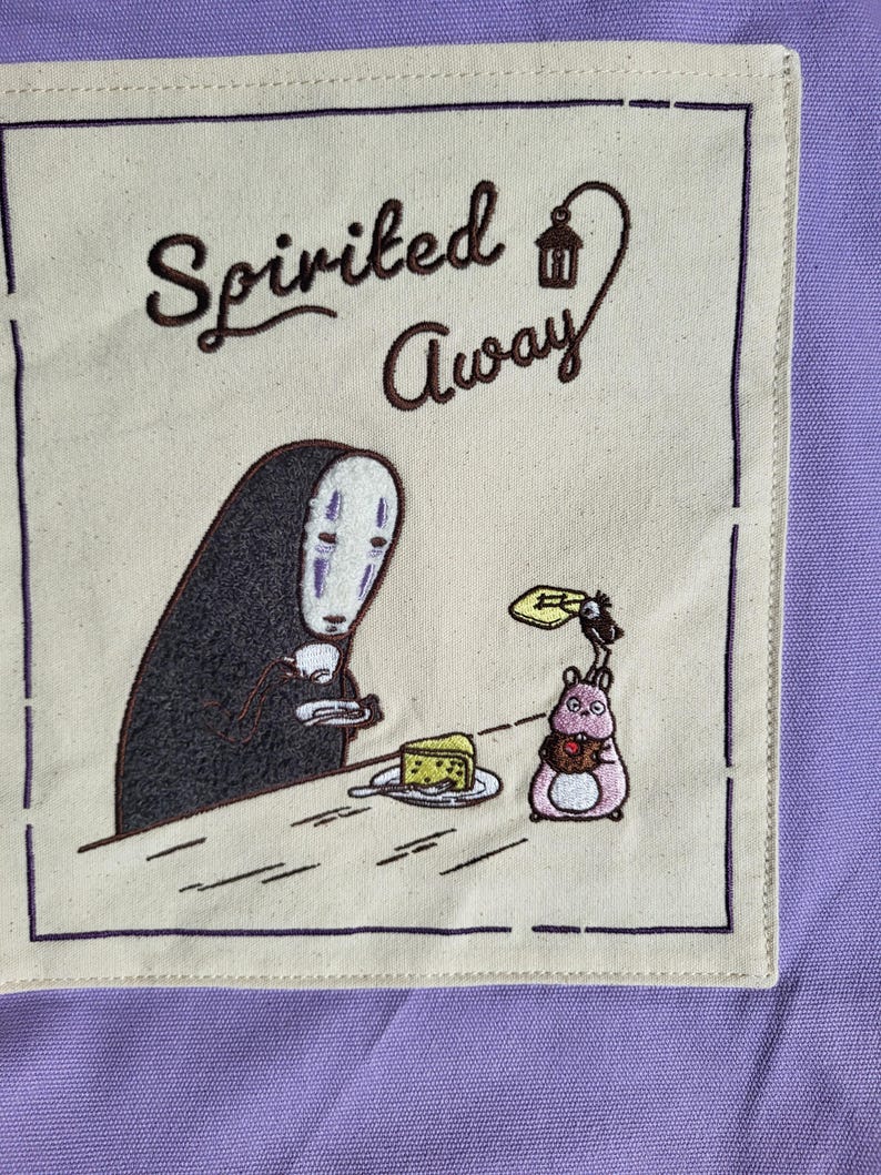 May include: A beige square patch with the words "Spirited Away" in brown script. The patch features an embroidered image of a character with a white mask and a black figure, a pink creature, and a slice of cake.