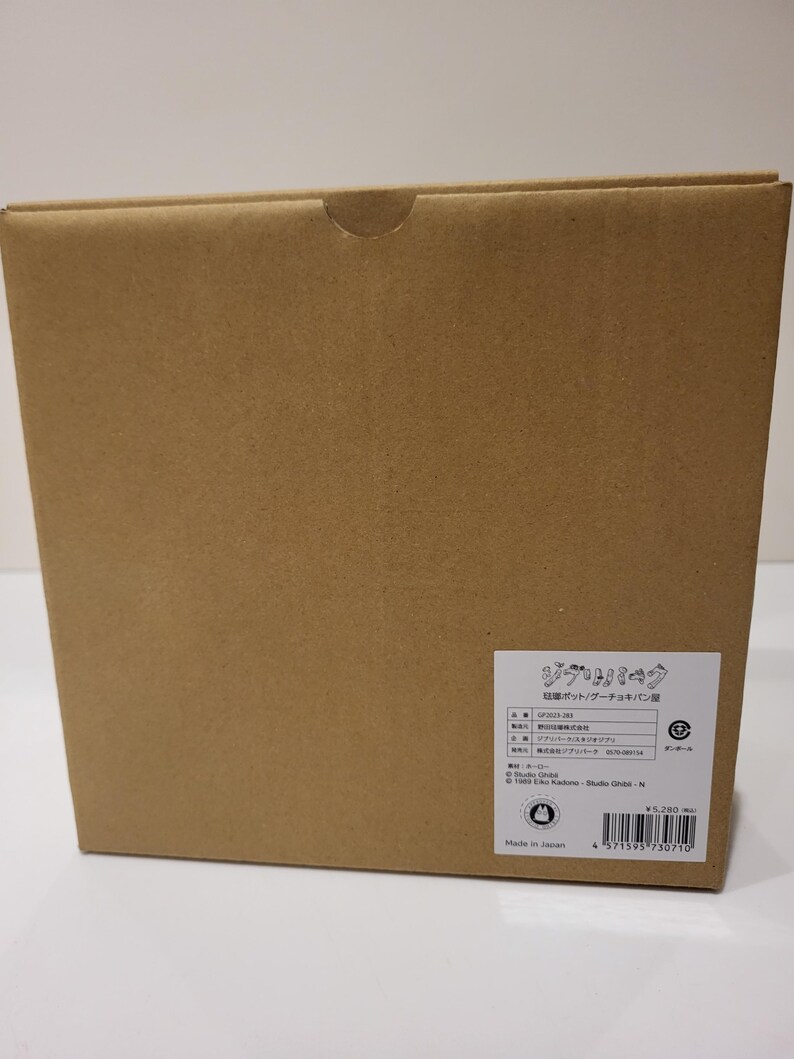 May include: A brown cardboard box with a white label and Japanese text. The box has a curved cutout on the top. The label includes the text "ジブリパーク" and a barcode.