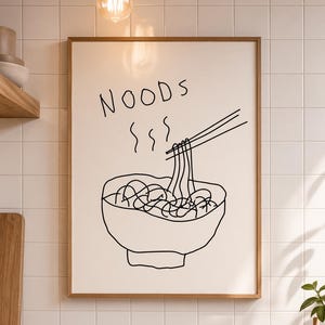 May include: A framed art print with a black line drawing of noodles in a bowl, with chopsticks. The word "NOODS" is written above the bowl in a handwritten style. The artwork is displayed on a white tiled wall.