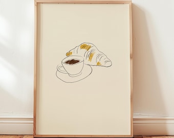 May include: A framed art print featuring a minimalist illustration of a coffee cup on a saucer and a croissant. The coffee cup is filled with dark liquid, and the croissant has yellow highlights. The artwork is set against a cream background.