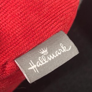 May include: A red fabric pillow with a gray tag that says "Hallmark" with a crown above the word.