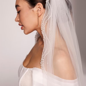 May include: A side profile of a person wearing a white wedding dress and veil. The veil is adorned with a delicate pearl trim. The text "PrincessVeil" is visible in the upper right corner.