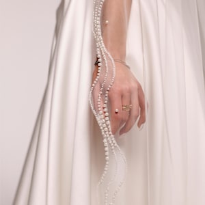 May include: A white bridal veil with a delicate pearl trim. The veil is held by a hand wearing a ring. The text "PrincessVeil" is visible on the veil.
