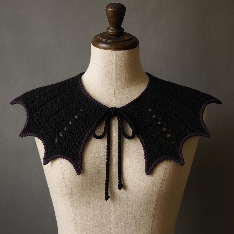 May include: A black crochet collar with bat wing-shaped edges and a purple trim. The collar has a tie closure and small decorative holes. The collar is displayed on a mannequin.