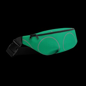 May include: A green fanny pack with a black zipper and strap. The fanny pack has a repeating pattern of large, light pink circles. The strap has a black buckle.