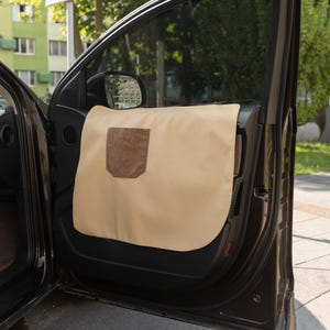 Puede incluir: Protector de puerta de coche beige con un bolsillo de ante marrón. El protector se fija en el interior de la puerta del coche y está diseñado para proteger la puerta de arañazos y suciedad.
