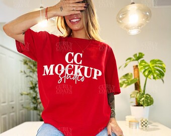 Könnte beinhalten: Ein rotes T-Shirt mit dem weißen Text "CC MOCKUP Studio". Das Model trägt eine hellblaue Jeans. Der Hintergrund umfasst eine Pflanze in einem weißen Topf und eine moderne Leuchte.