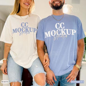 May include: Two people wearing matching t-shirts. One shirt is white, the other is light blue. Both shirts have the text "CC MOCKUP Studio" in a blue font. The models are wearing blue jeans.