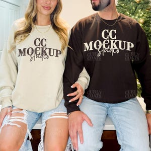 May include: Two sweatshirts, one beige and one brown, with the text "CC MOCKUP Studio" in white. The beige sweatshirt is paired with light blue ripped jeans. The brown sweatshirt is paired with light blue jeans. The sweatshirts are from Curly Coats.