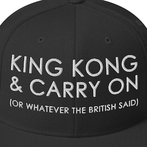 May include: Black baseball cap with the embroidered text "KING KONG & CARRY ON (OR WHATEVER THE BRITISH SAID)". The cap has a flat brim and a structured crown. The text is in white, contrasting against the black fabric.