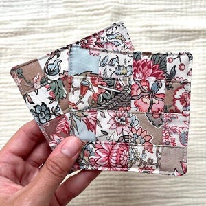 Puede incluir: Conjunto de dos posavasos de tela con un diseño de patchwork que presenta motivos florales en tonos rosa, azul y marrón.