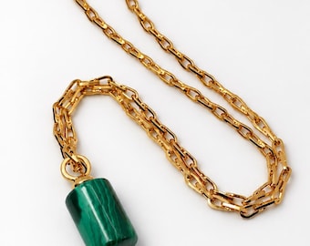 May include: A gold-toned chain necklace featuring a cylindrical pendant made of green malachite with distinct dark green banding. The pendant is capped with a small gold-toned metal accent at the bottom and attached to the chain with a gold ring.