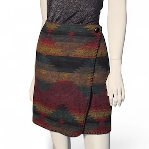 May include: A wrap skirt with a Southwestern-inspired pattern in shades of red, brown, green, and yellow. The skirt has a button closure and a stitched hem. The skirt is displayed on a mannequin.