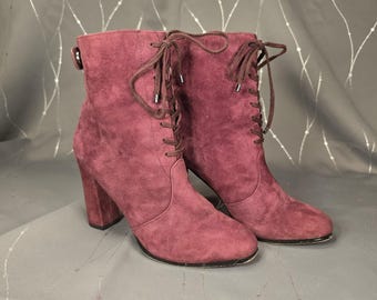 May include: A pair of burgundy suede ankle boots with a lace-up design. The boots have a block heel and a side buckle. The laces and heel are a darker shade of burgundy. The boots are approximately 6 inches tall.