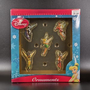 May include: A Disney branded box containing five individual fairy ornaments. The packaging is blue and red with snowflake patterns and the word Ornaments printed at the bottom. Each ornament features a different fairy with wings in various poses.