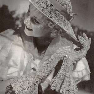 May include: A woman wearing a white crocheted hat and matching gloves. The hat has a wide brim and a delicate lace pattern. The gloves are long and have a similar lace pattern.