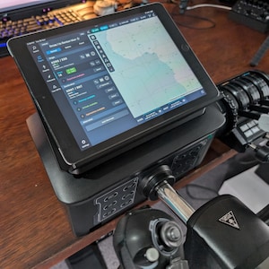 Könnte beinhalten: Ein schwarzes Bedienfeld mit einem darauf montierten Tablet. Das Tablet zeigt eine Karte mit einem blauen Bereich und weißen Linien. Das Bedienfeld hat einen silbernen Hebel mit einem schwarzen Knopf. Das Bedienfeld hat ein schwarzes und silbernes Design mit einem silbernen Logo.