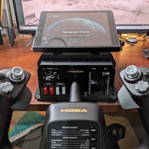May include: A black Moza flight simulation yoke and throttle quadrant system featuring a central control unit with switches, levers, and a tablet mounted on top displaying the Navigraph Charts interface with a globe graphic and text.