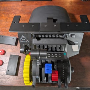 May include: A black flight simulator control panel with a variety of buttons, switches, and knobs. The panel is mounted on a black metal frame. The panel is labeled "FLAPS" and "GEAR".