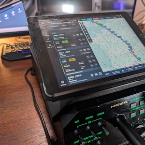May include: A black tablet displaying flight information, mounted on a black control panel with the brand name "MOZA". The panel has various switches and knobs labeled "NAV", "BEACON", and "FUEL PUMP". A computer monitor and keyboard are visible in the background.