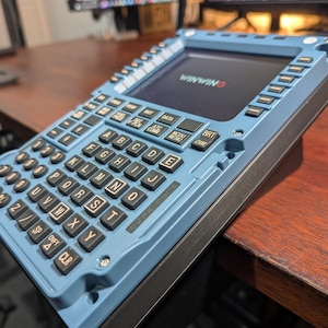 May include: A light blue electronic device with a keyboard and screen, displaying the text "WINWING". The device has black keys with white lettering and various function buttons. It rests on a dark surface.