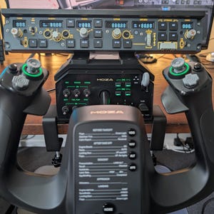 Peut inclure: Un panneau de commande de simulateur de vol noir avec plusieurs boutons, molettes et écrans numériques. Le panneau est monté au-dessus d'une unité de contrôle MOZA et flanqué de deux manches à balai noirs avec des accents verts. Le bas comporte un volant.