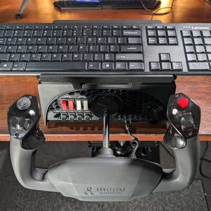 May include: A black keyboard with a numeric keypad is mounted on a black metal stand. The stand is attached to a black and gray flight simulator joystick with red and white buttons. The joystick has the text "Honeycomb Aeronautical" printed on it.