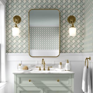 May include: A bathroom vanity with a gold-framed mirror, gold fixtures, and two sconces. The vanity is light green with a marble countertop. The wallpaper has a repeating pattern of light green and white shapes.