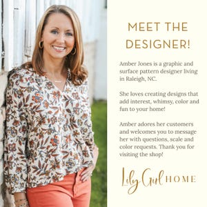 May include: A smiling woman wearing a floral print blouse and orange pants. The text reads "MEET THE DESIGNER!" and introduces Amber Jones, a graphic and surface pattern designer. The shop name "Lily Girl HOME" is also displayed.