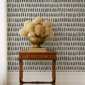 May include: A wooden side table with a drawer and a brass bowl filled with dried flowers. The table is set against a wall with a cream background and a pattern of navy blue brushstrokes.
