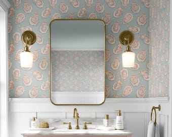 May include: A bathroom with a pink vanity, gold fixtures, and a large rectangular mirror. The walls are decorated with wallpaper featuring a pattern of pink and white oyster shells on a light blue background. Two gold sconces flank the mirror.
