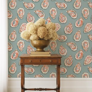 May include: A room featuring a teal oyster-patterned wallpaper. A small, dark wooden table holds a brass bowl filled with dried flowers and a stack of books. The wallpaper design includes oyster illustrations in shades of pink, orange, and blue.