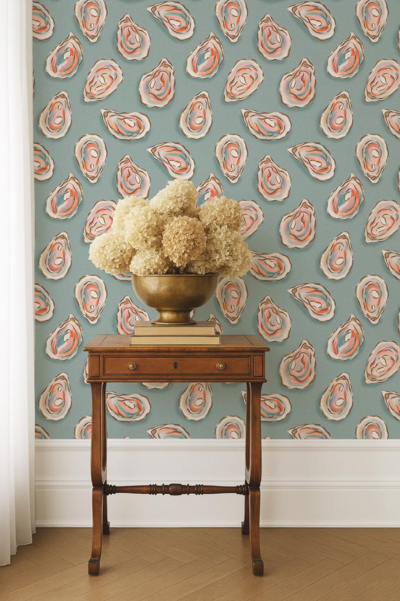 May include: A room featuring a teal oyster-patterned wallpaper. A small, dark wooden table holds a brass bowl filled with dried flowers and a stack of books. The wallpaper design includes oyster illustrations in shades of pink, orange, and blue.