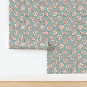 May include: Wallpaper featuring a repeating pattern of oyster shells in shades of pink, orange, and blue on a muted teal background. The design is a watercolor style, with each shell slightly different. The wallpaper is shown partially rolled out.