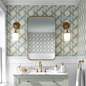 May include: A bathroom vanity with a white countertop and a light green cabinet. The vanity has a gold faucet and two gold sconces with white glass shades. The walls are covered in a light green and white geometric wallpaper.