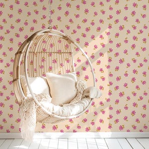 May include: A white wicker hanging chair with a cream-colored cushion and throw blanket, set against a wall with a pink and gold floral pattern wallpaper.