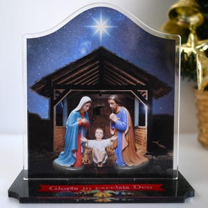 Könnte beinhalten: Eine Weihnachtskrippe mit Maria, Josef und dem Jesuskind in einem Stall. Die Figuren befinden sich in einem transparenten Acrylrahmen mit Sternenhimmel-Hintergrund und dem Text "Gloria in excelsis Deo" auf dem Sockel.