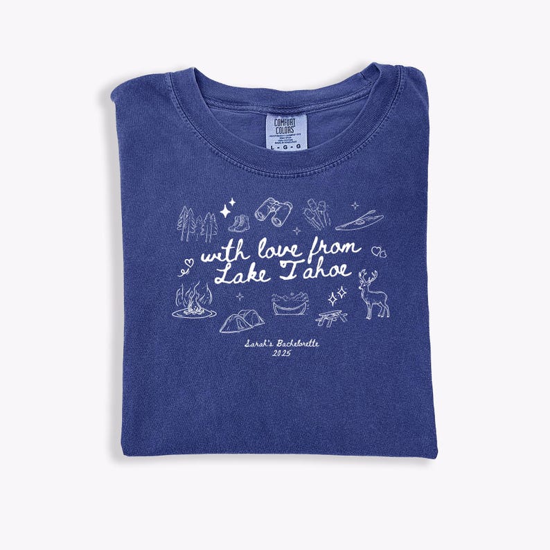 May include: A blue Comfort Colors t-shirt with a white graphic design. The design includes trees, binoculars, a campfire, a tent, and the text "with love from Lake Tahoe" and "Sarah's Bachelorette 2025".