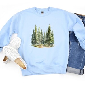 May include: Light blue sweatshirt with a watercolor illustration of a forest path with trees on the front.