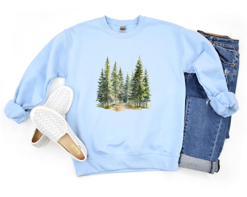 May include: Light blue sweatshirt with a watercolor illustration of a forest path with trees on the front.