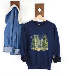 May include: Navy blue sweatshirt with a watercolor illustration of a forest scene with pine trees and a snowy background.