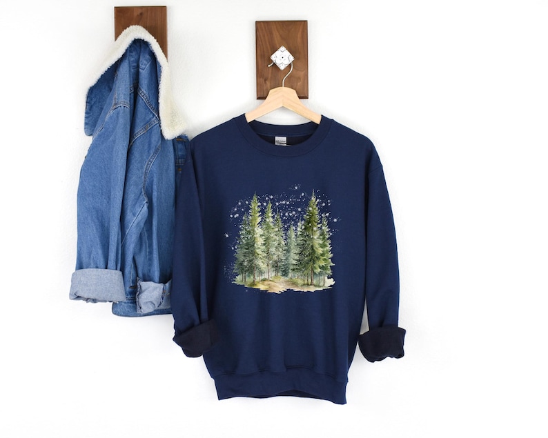 May include: Navy blue sweatshirt with a watercolor illustration of a forest scene with pine trees and a snowy background.