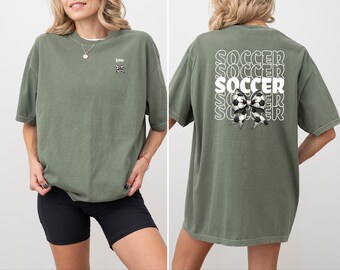 Könnte beinhalten: Zwei grüne T-Shirts mit unterschiedlichen Designs. Ein Shirt hat das Wort "John" und einen Fußball mit einer Schleife. Das andere Shirt hat das Wort "Soccer" fünfmal wiederholt mit einem Fußball mit einer Schleife in der Mitte.