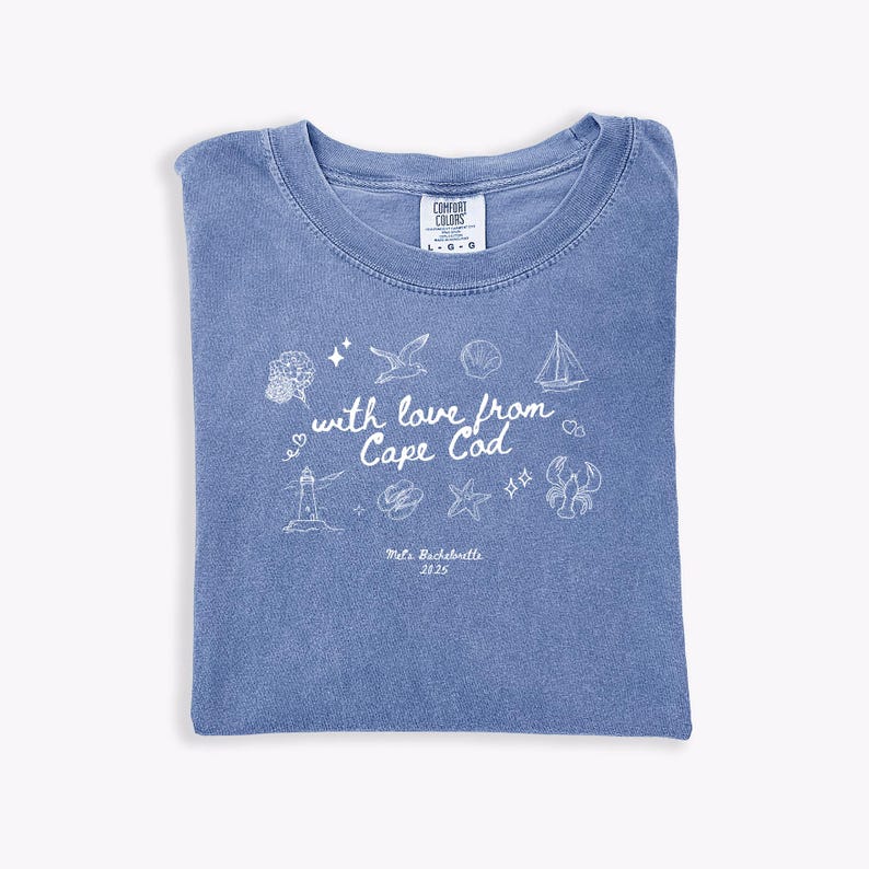 May include: A blue t-shirt with a crew neck, featuring white illustrations of a lighthouse, sailboat, and other coastal elements. The text "with love from Cape Cod" and "Mels Bachelorette 2025" are also printed on the shirt.