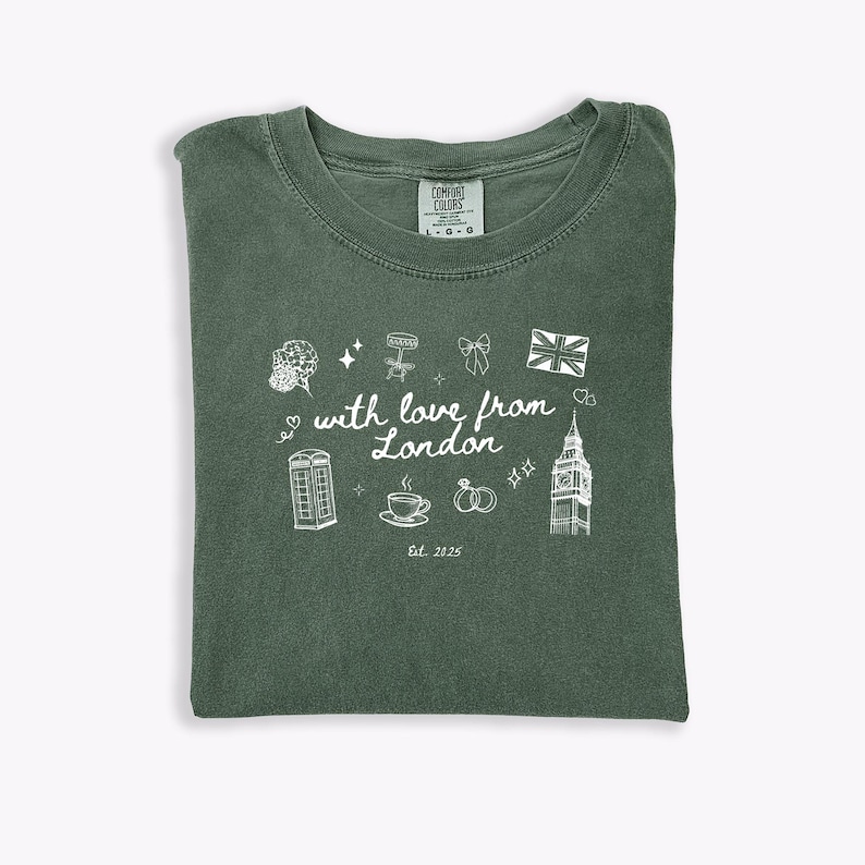May include: Green Comfort Colors t-shirt with a white graphic design. The design includes a bouquet, stars, a bow, a Union Jack, a phone booth, a cup of tea, wedding rings, Big Ben, and the text "with love from London" and "Est. 2025".